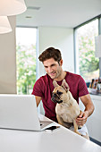 Man using laptop with dog on lap