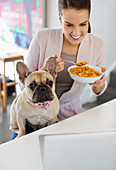 Woman eating cereal with dog on lap