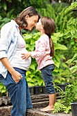 Girl kissing pregnant mother outdoors