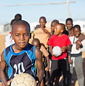 Boys holding soccer balls in dirt field