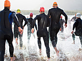 Triathletes in wetsuits running in waves