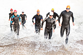 Triathletes in wetsuits running in waves