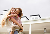 Mother and daughter hugging outside house