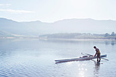 Man placing rowing scull in lake