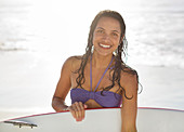 Smiling woman holding surfboard on beach