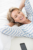 Older woman listening to earphones on bed