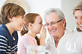Girl whispering to grandfather at table
