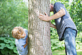 Father and son peeking around tree