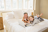 Father and daughter using laptop on bed