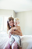 Children using cell phone together on bed