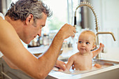 Father bathing baby in kitchen sink