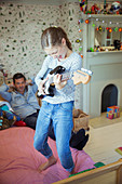 Girl playing guitar for father in bedroom