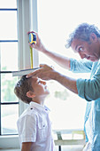 Father measuring son's height on wall