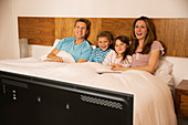 Family watching television in bed