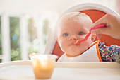 Mother feeding baby girl in high chair