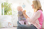 Mother playing with baby girl on sofa