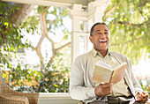 Laughing senior man reading book on porch