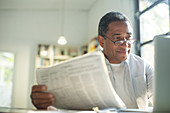 Senior man with newspaper using laptop