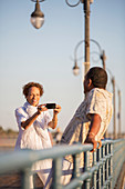 Woman photographing man on pier