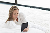 Woman in bathrobe using tablet in bedroom