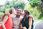 Women kissing man's cheeks outdoors