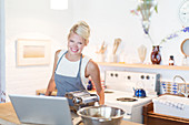 Woman at laptop cooking in kitchen