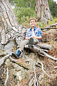 Boy sitting on tree roots in forest