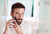 Man trimming beard in bathroom mirror
