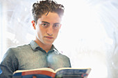 Student with book standing beside window