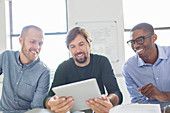 Three smiling men working with tablet