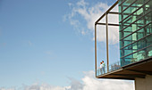 Men standing on balcony of glass bump out against blue sky
