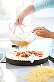 Woman preparing tomato quiche in kitchen