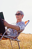 Senior woman reading book in sunny field