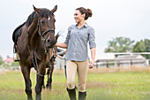 Woman walking horse in rural pasture