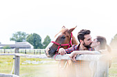 Couple with horse kissing fence