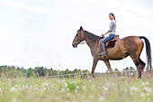 Woman horseback riding in rural field