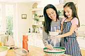 Mother and daughter baking sifting flour