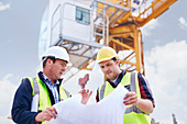 Worker reviewing blueprints below crane