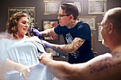 Tattoo artist tattooing woman's shoulder