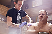 Tattoo artist tattooing man's shoulder