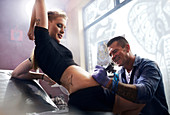 Tattoo artist tattooing woman's stomach