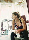 Woman with water bottle resting at gym
