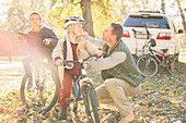 Father fastening helmet of son on bicycle