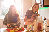 Girls making smoothie in sunny kitchen