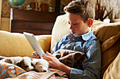 Boy using tablet with puppies in lap