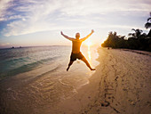 Man jumping on tropical beach at sunset