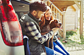 Couple petting pet dog at back of car