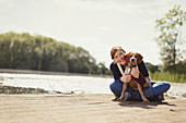 Woman hugging dog on sunny lakeside dock