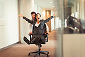 Businessman pushing businesswoman in office chair