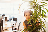 Businesswoman hiding behind plant in office